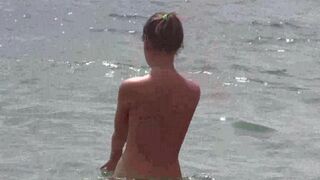 A group of naked beauties relax on the sandy beach and sunbathe