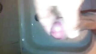 The kid caresses his dick with his hand while standing in the shower stream