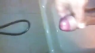 The kid caresses his dick with his hand while standing in the shower stream